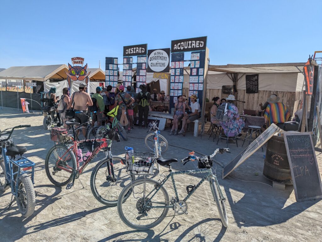 A wide shot of the front of our camp at Burning Man. There are bikes in the foreground and a crowd of people around the camp frontage.